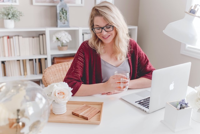 A smiling woman enjoying a cup of tea while working on her desk