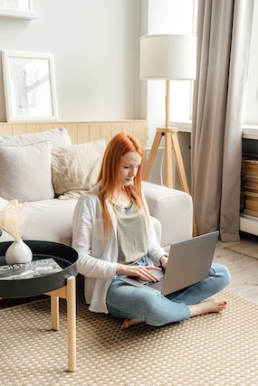 A woman typing on her laptop while sitting on the floor at home