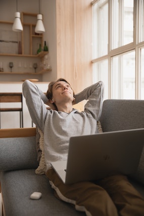 A guy stretching on the couch with his laptop on his knees