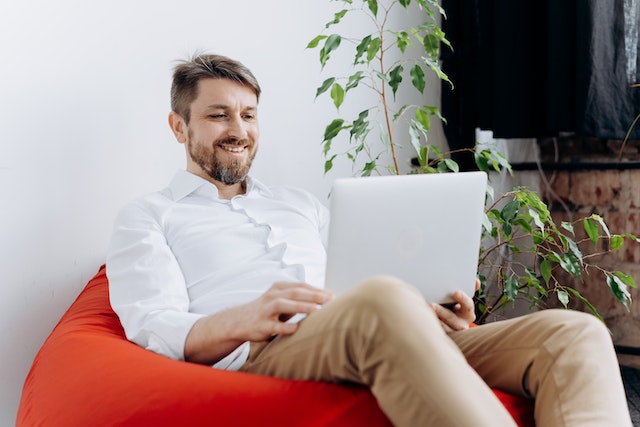 A man comfortably sat on a bean bag on the floor at home while working