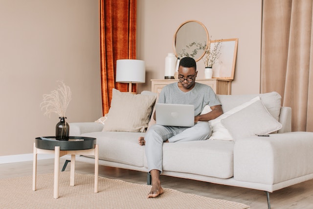 A buy using his laptop while casually sitting on his couch at home